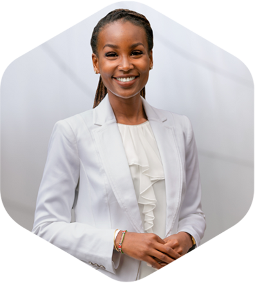 A professional woman in a white suit and tie stands confidently in front of a wall.