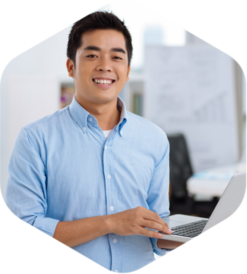 An Asian man in an office, holding a laptop, focused on his work.